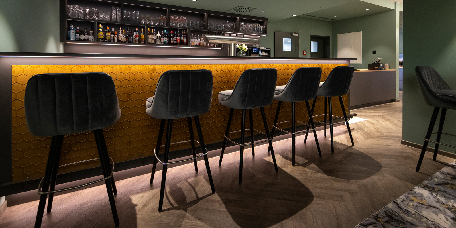 zieflekoch hotel fulda mitte graue dekorflaechen holzflaechen kastanie goldfarben schallschutzoberflaechen wabenform gruentoene wandbilder sessel hocker tische polsterbaenke restaurant bar lounge marmoroptik