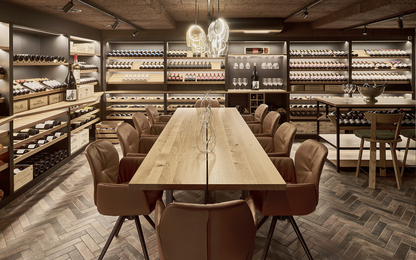 A modern wine cellar featuring a long wooden table surrounded by leather chairs. Walls lined with wooden shelves display numerous bottles of wine. Soft, ambient lighting creates a warm atmosphere. The design emphasizes elegance and sophistication, making it suitable for wine tasting or gatherings.