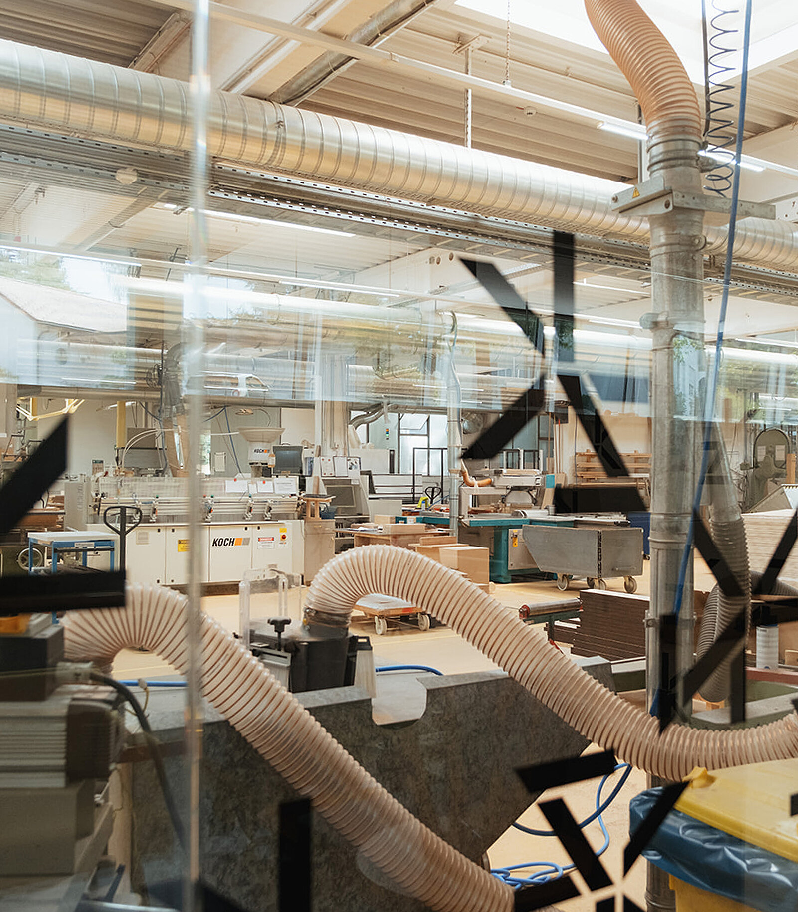 Eine moderne Werkstatt mit verschiedenen Maschinen und Werkzeugen. Flexible Schläuche sind sichtbar, die möglicherweise zur Absaugung von Holzspänen verwendet werden. Die Umgebung wirkt industriell und gut organisiert, ideal für handwerkliche Arbeiten.