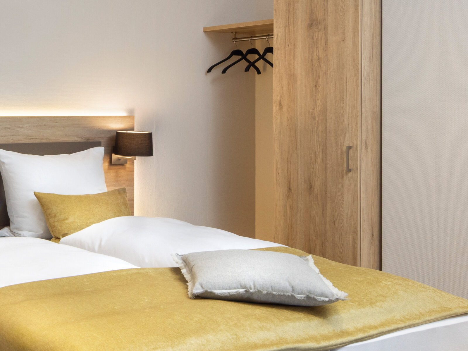 zieflekoch musterzimmer zaris, modernes Zimmer mit einem Doppelbett, gelben Akzenten, einem grauen Sofa, abstrakter Wandkunst und einem Holzschrank, die warme Beleuchtung schafft eine gemütliche Atmosphäre