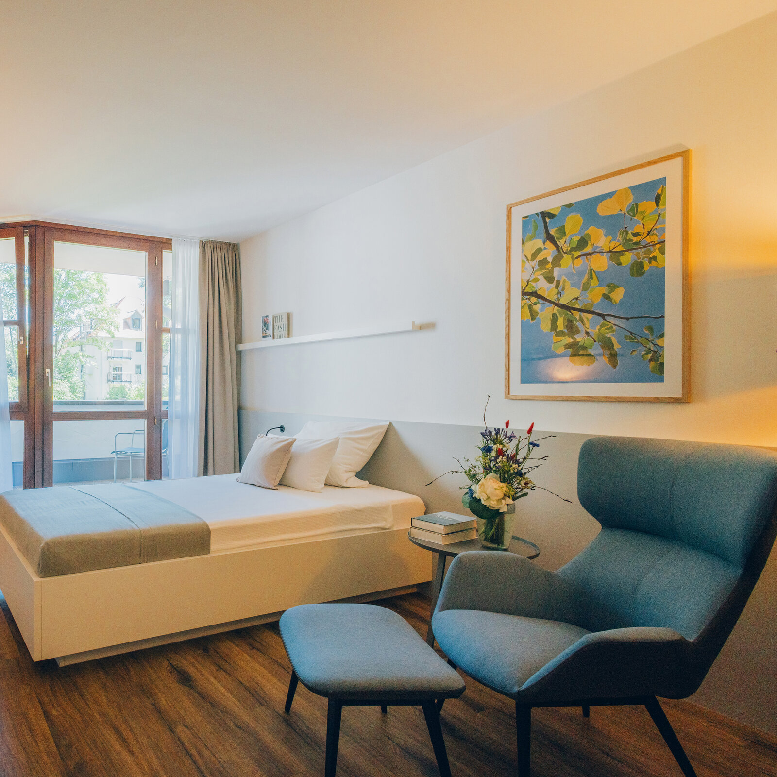 Patientenzimmer mit Balkonzugang, Tür aus Eiche, Polstersessel in blau, Einzelbett