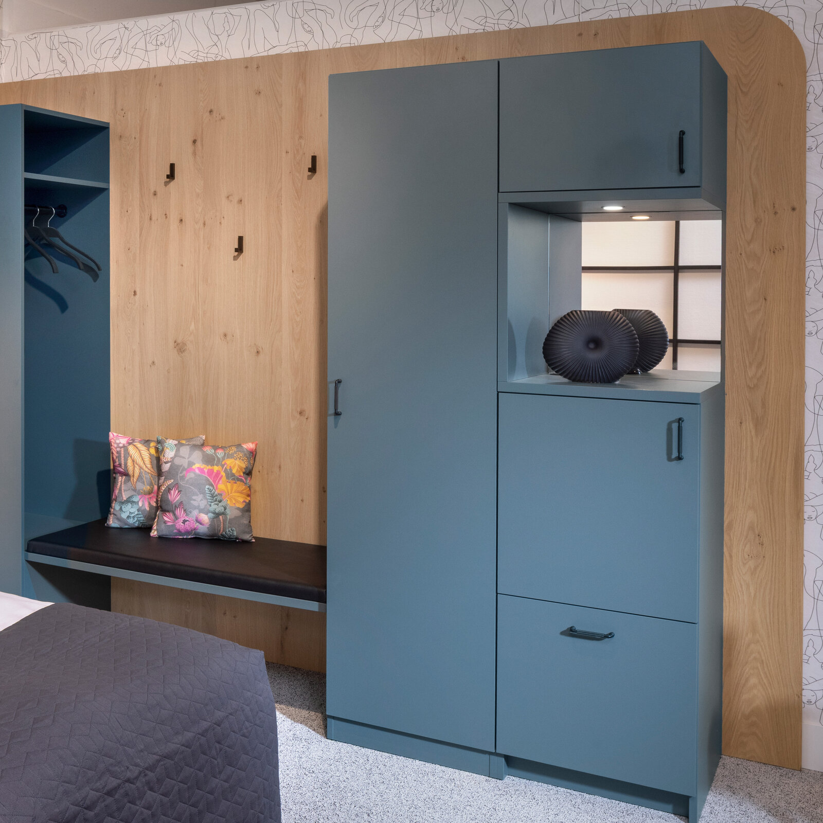 zieflekoch musterzimmer zenit, Zimmer mit Kleiderschrank in gedecktem Grünton, abgerundete Holzvertäfelung, Blumenkissen auf einer Bank und einer dekorativen Vase. Neutrale Töne und schlichtes Design