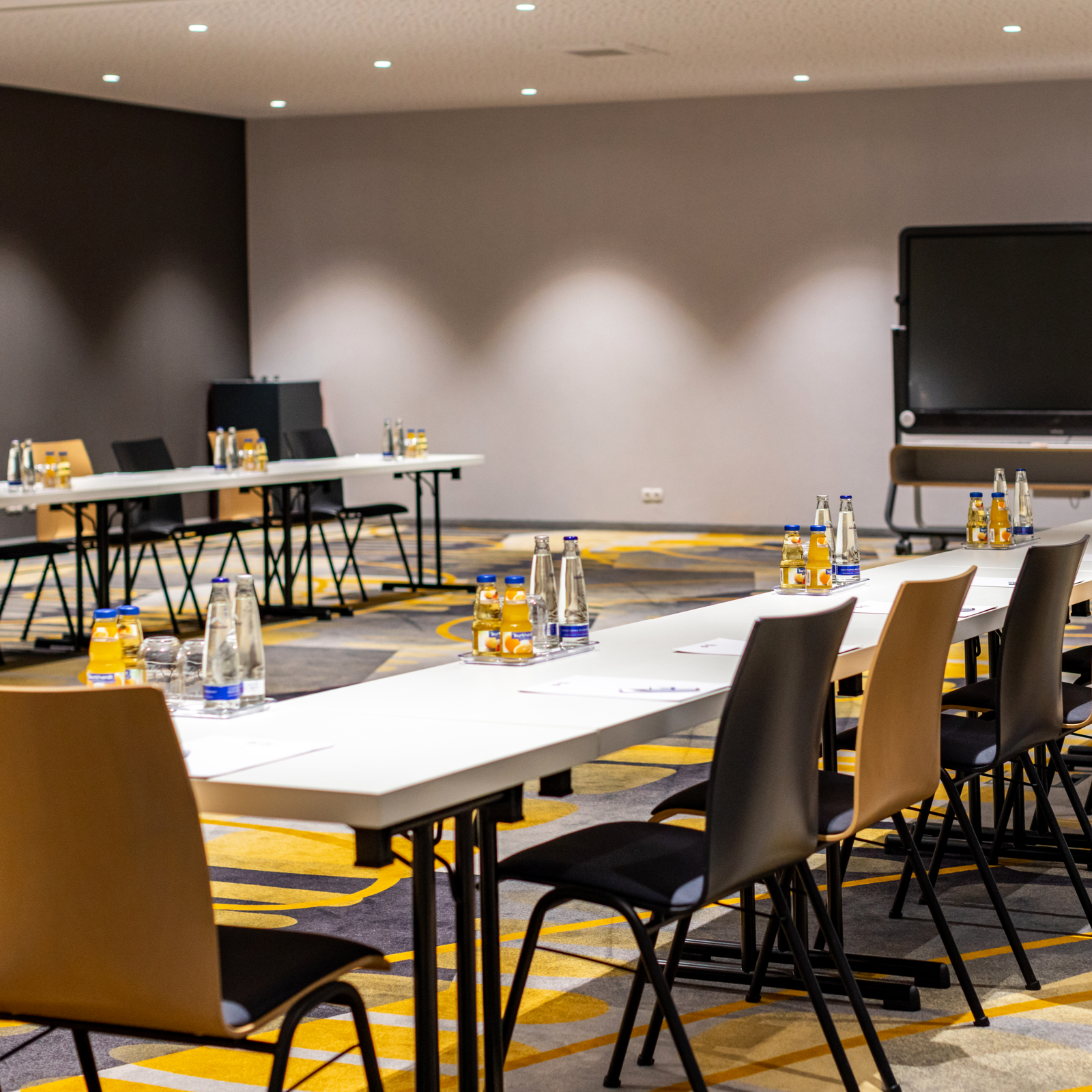 zeiflekoch hotel maximilian parkhotel, moderner konferenzraum mit tischen aufgestellt in U-Form, holzstühle mit gepolsterter sitzfläche, großer monitor an der wand montiert