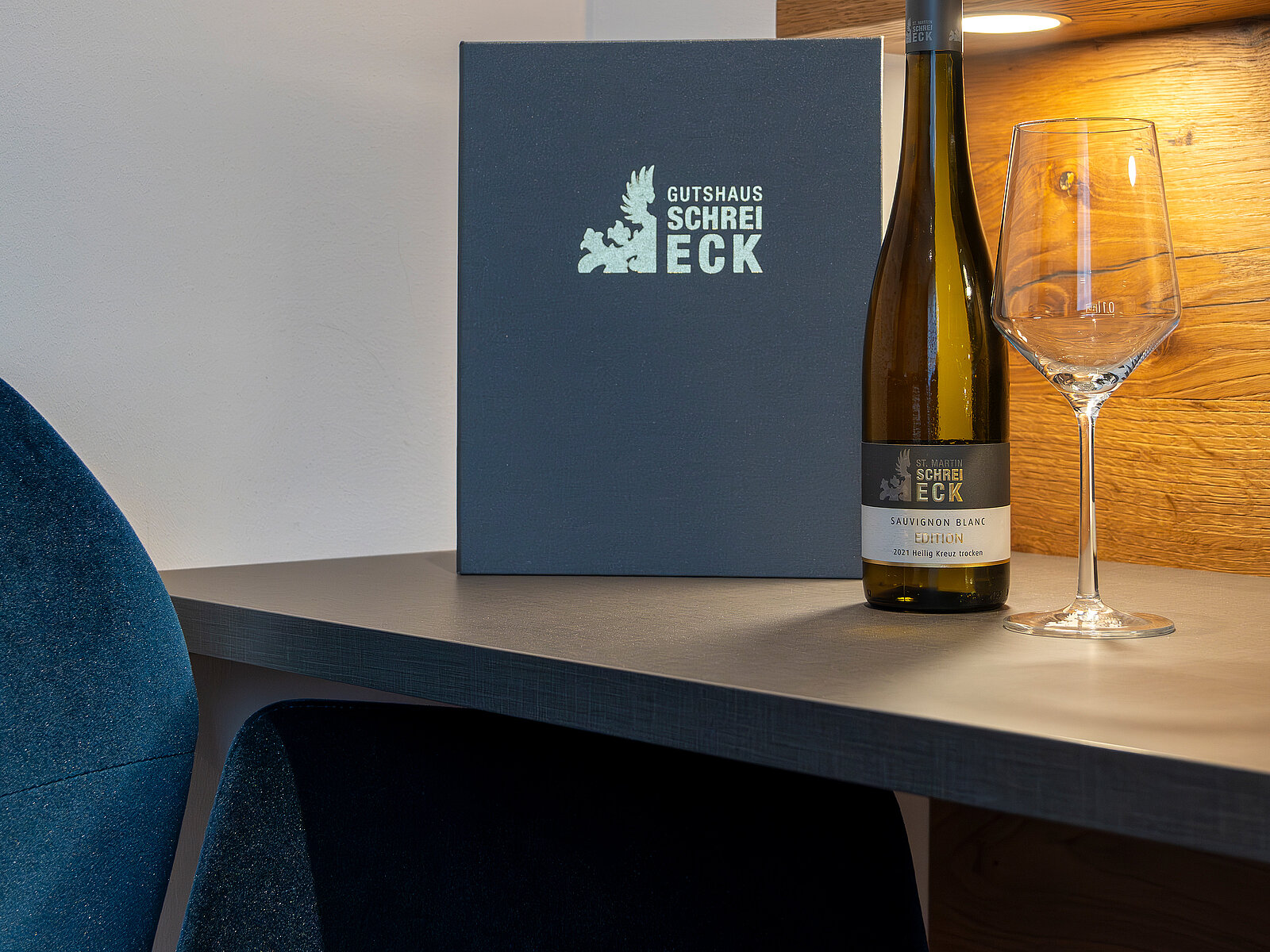 Auf einem Tisch stehen eine Flasche Wein und ein Weinglas. Neben der Flasche liegt eine schwarze Menükarte mit dem Schriftzug "Gutshaus Schreieck". Die Szene strahlt eine elegante und einladende Atmosphäre aus.