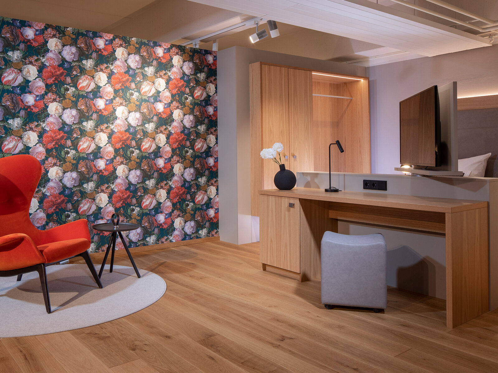 zieflekoch musterzimmer ziloft zimmer holz sessel schrank einbauschrank tapete blumenmuster hocker schreibtisch schreibtischlampe beistelltisch indirekte beleuchtung tv schwenkbar drehbar teppich