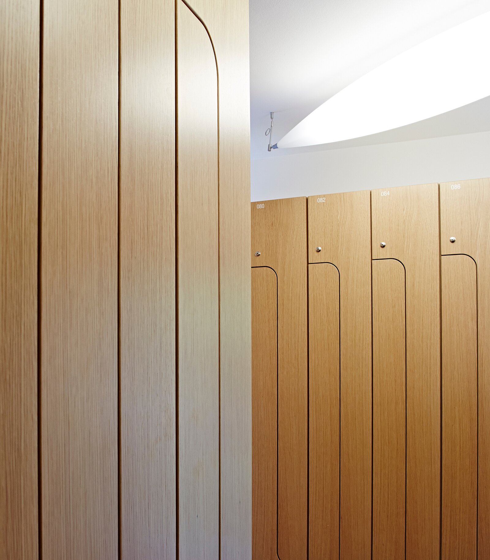 Das Bild zeigt einen Bereich mit Holzschränken, die Reihe für Reihe angeordnet sind. Die Schränke sind hellbraun und mit glatten Oberflächen gestaltet. Eine indirekte Beleuchtung von oben sorgt für ein sanftes Licht im Raum.