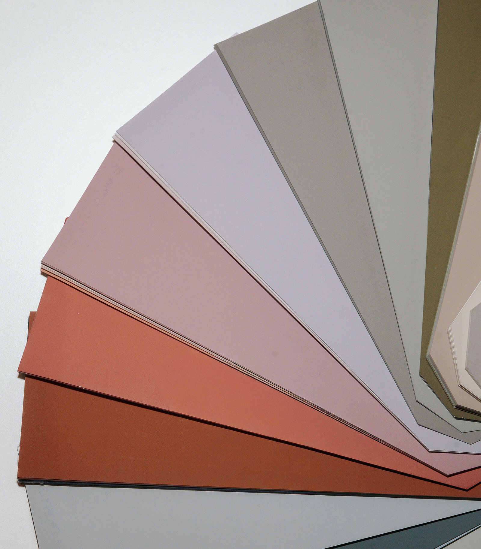 Eine Farbpalette mit verschiedenen Farbtönen, die in einem Fächer angeordnet sind. Die Farben reichen von sanften Rosa- und Grautönen bis zu erdigen Rot- und Grüntönen. Diese Palette könnte für Gestaltung oder Farbauswahl verwendet werden.