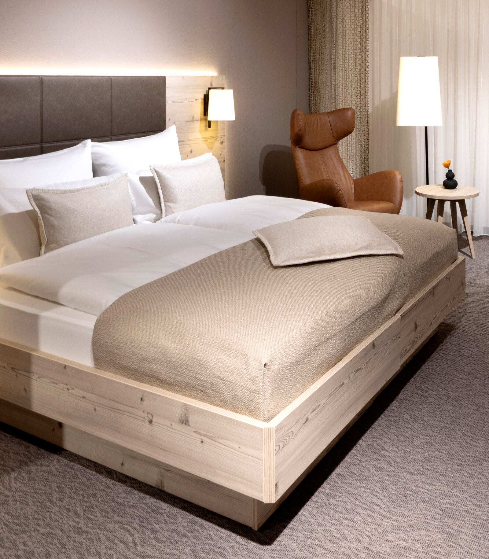 Hotelzimmer mit Doppelbett aus astiger Silberkiefer mit braunem Ledersessel