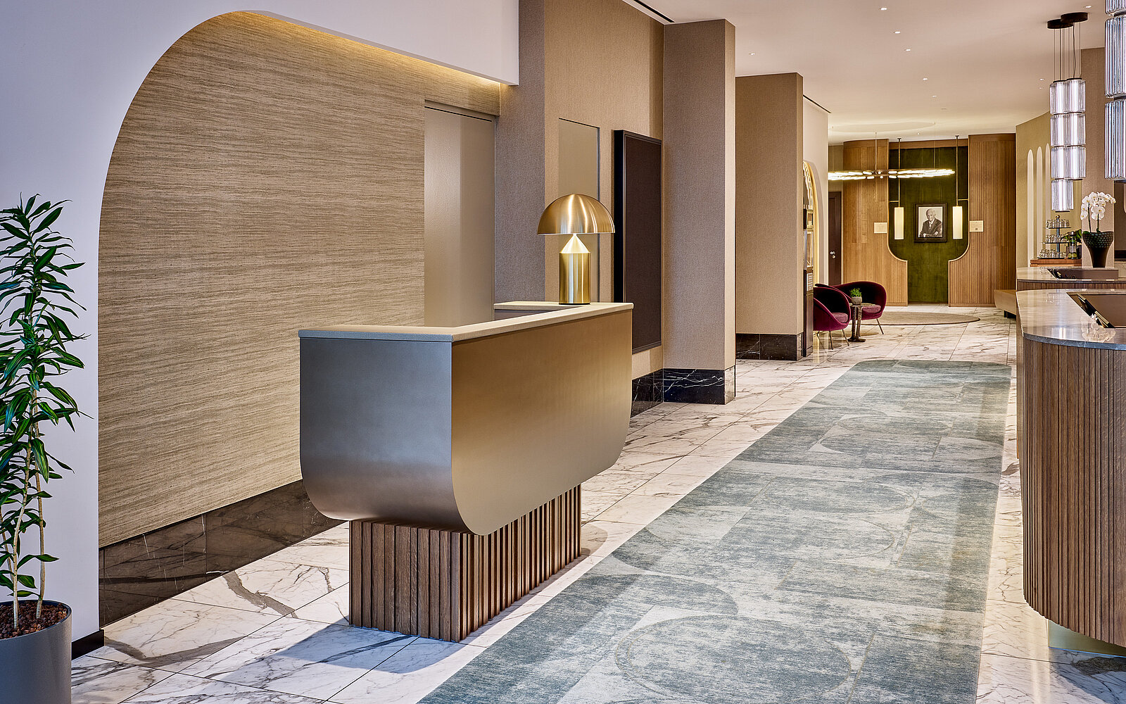 Ein eleganter, moderner Empfangsbereich mit einem stilvollen Empfangstresen aus Metall und Holz. Der Boden ist mit Marmorfliesen und einem blauen Teppich gestaltet. Dezente Beleuchtung und minimalistische Möbel schaffen eine einladende Atmosphäre.