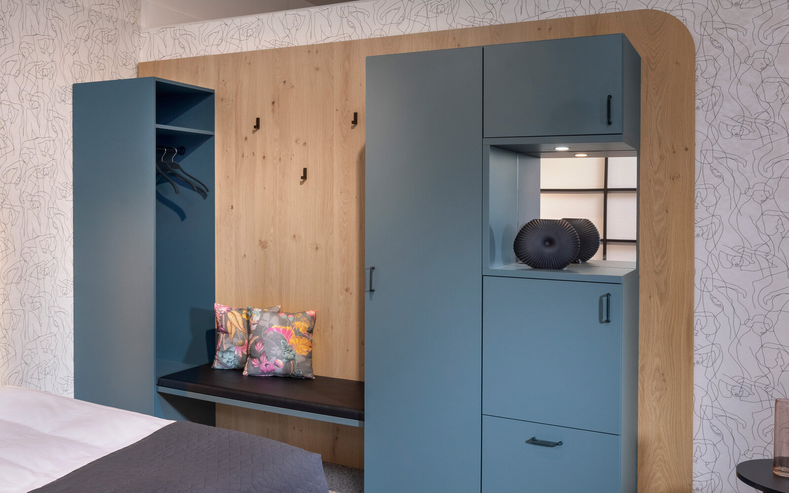 zieflekoch musterzimmer zenit, Zimmer mit Kleiderschrank in gedecktem Grünton, abgerundete Holzvertäfelung, Blumenkissen auf einer Bank und einer dekorativen Vase. Neutrale Töne und schlichtes Design