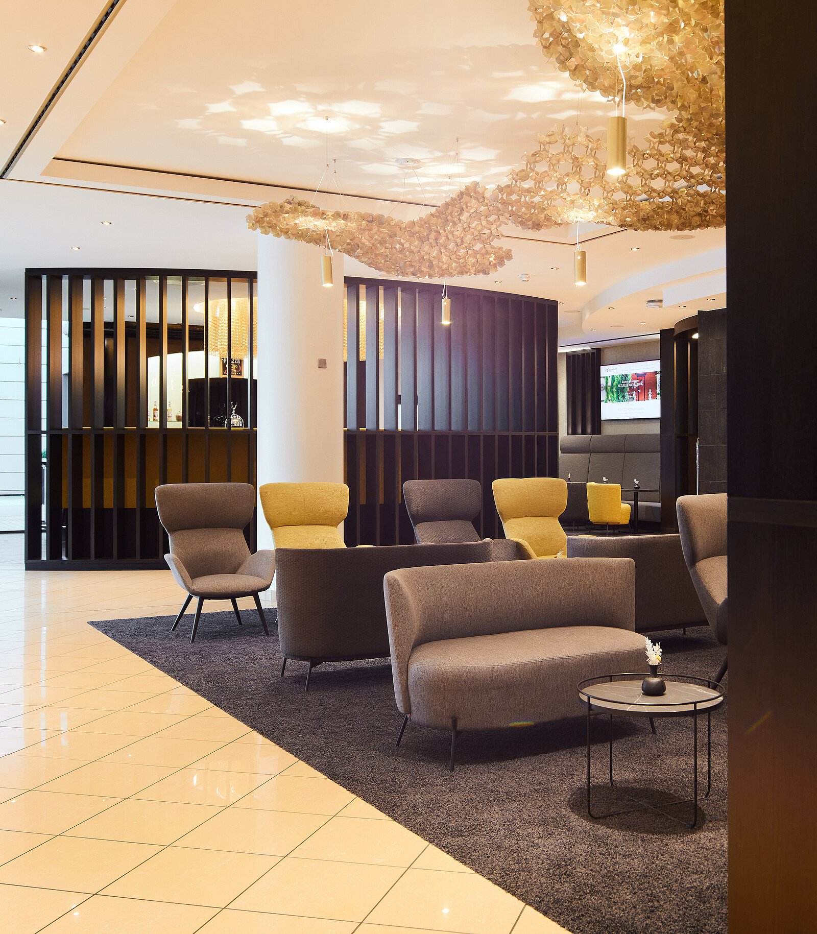 Empfangsbereich des Hotel Esperanto mit gelben und Grauen Sitzmöglichkeiten und goldener detailreicher Deckenbeleuchtung
