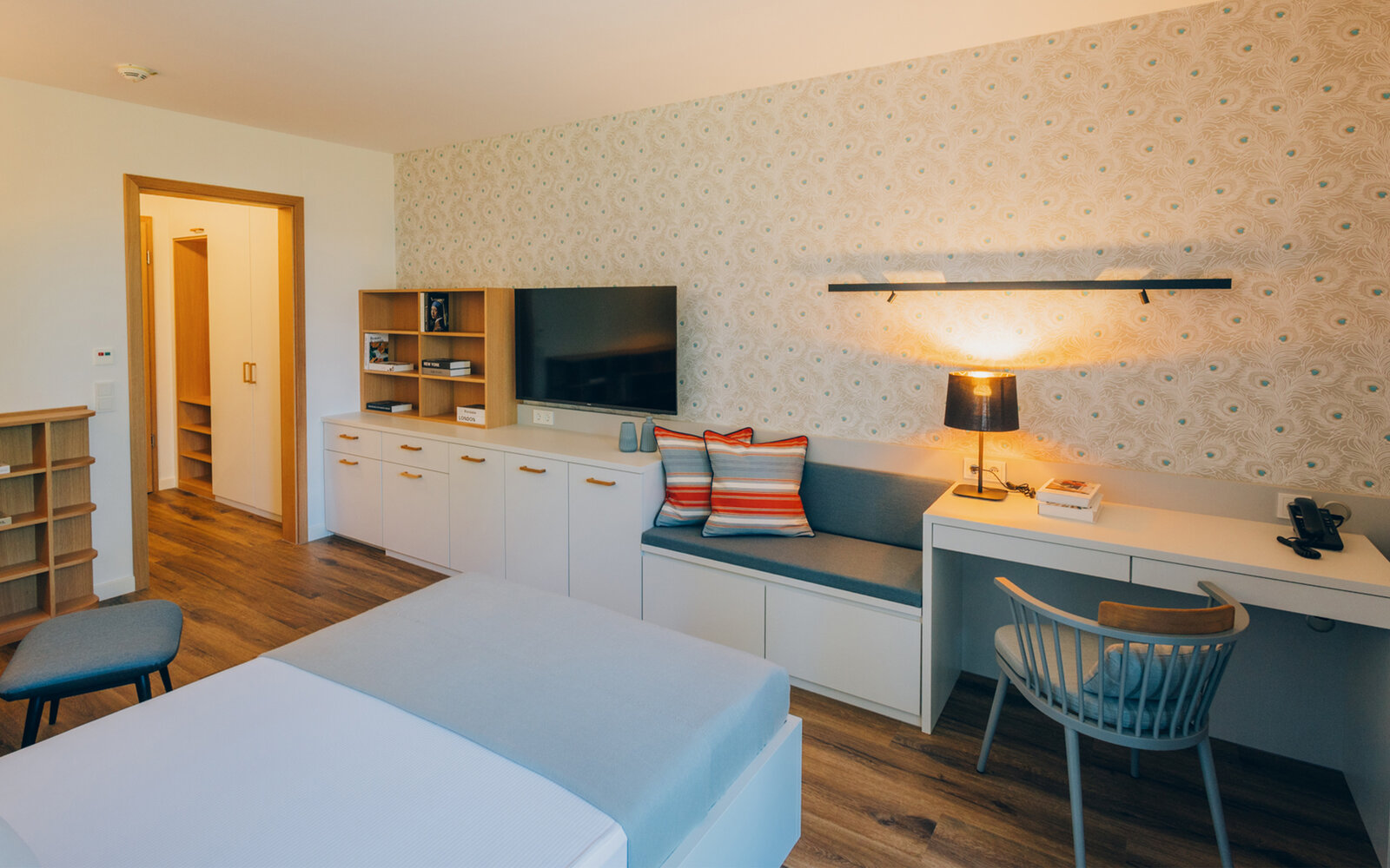 Patientenzimmer in einer Fachklinik mit dezente blau gemusterten Tapete und weißem Sideboard