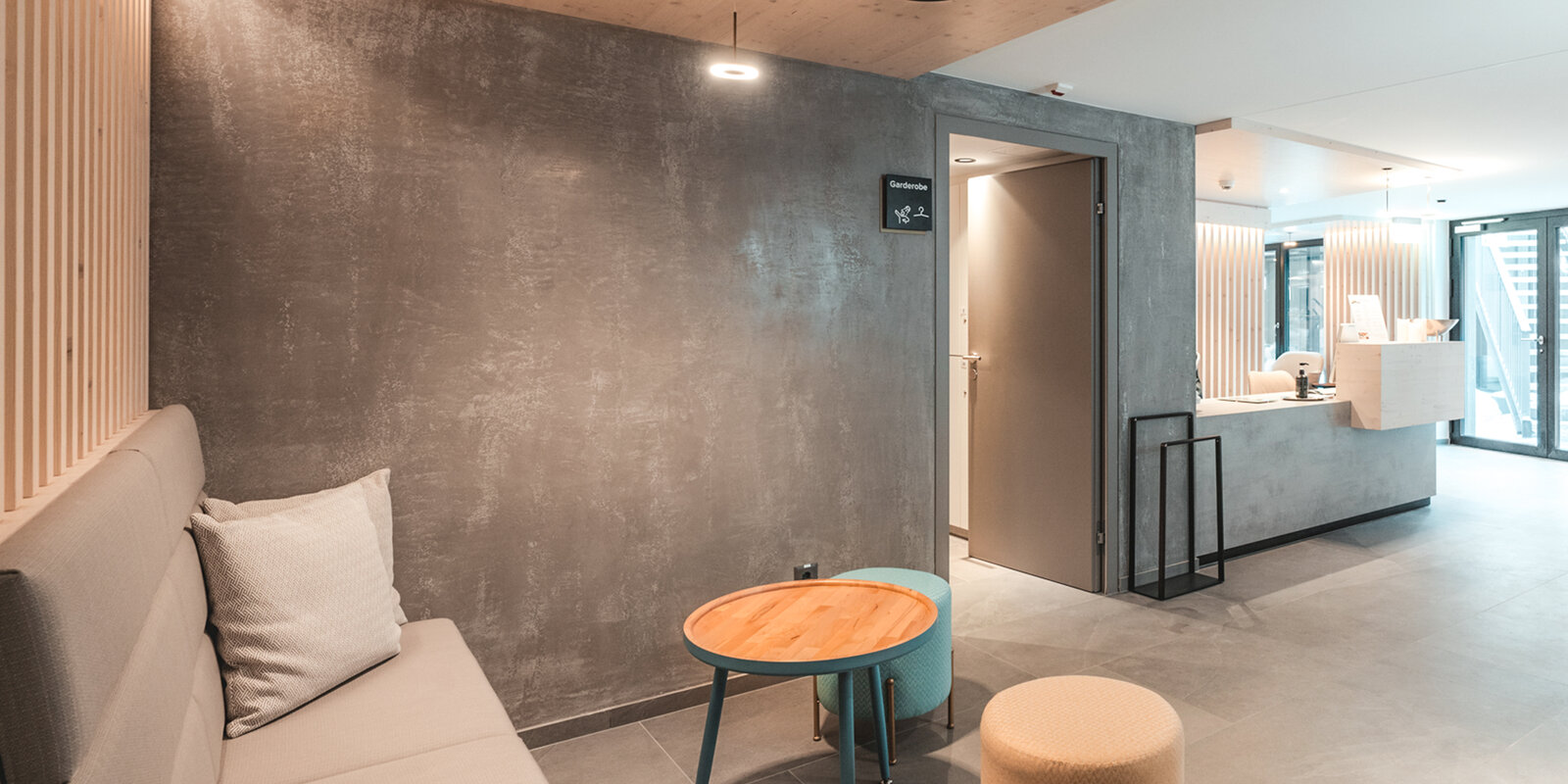 zieflekoch Alpen Resort Empfang Rezeption Lobby Holzwand Holz Sitzbank Sitzecke Beton