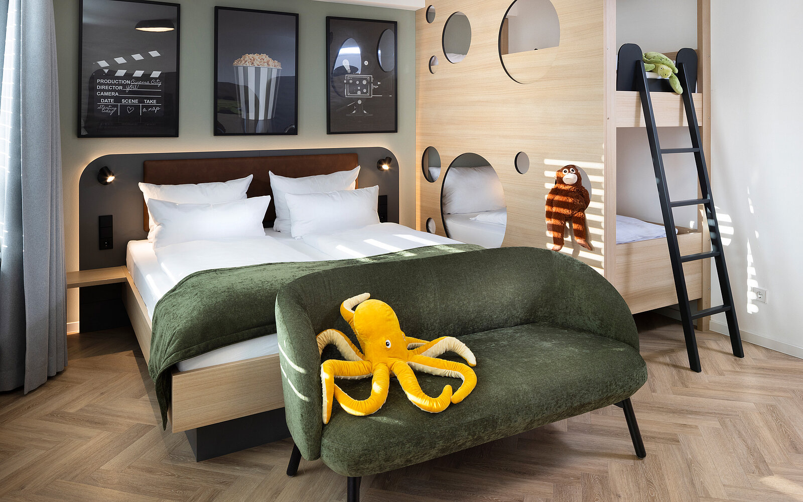 A cozy children's bedroom featuring a large bed with white linens and a green throw blanket. A sofa with a yellow octopus plush toy sits in front. In the background, there are playful decor elements, including a bunk bed and framed movie-themed artwork on the walls.