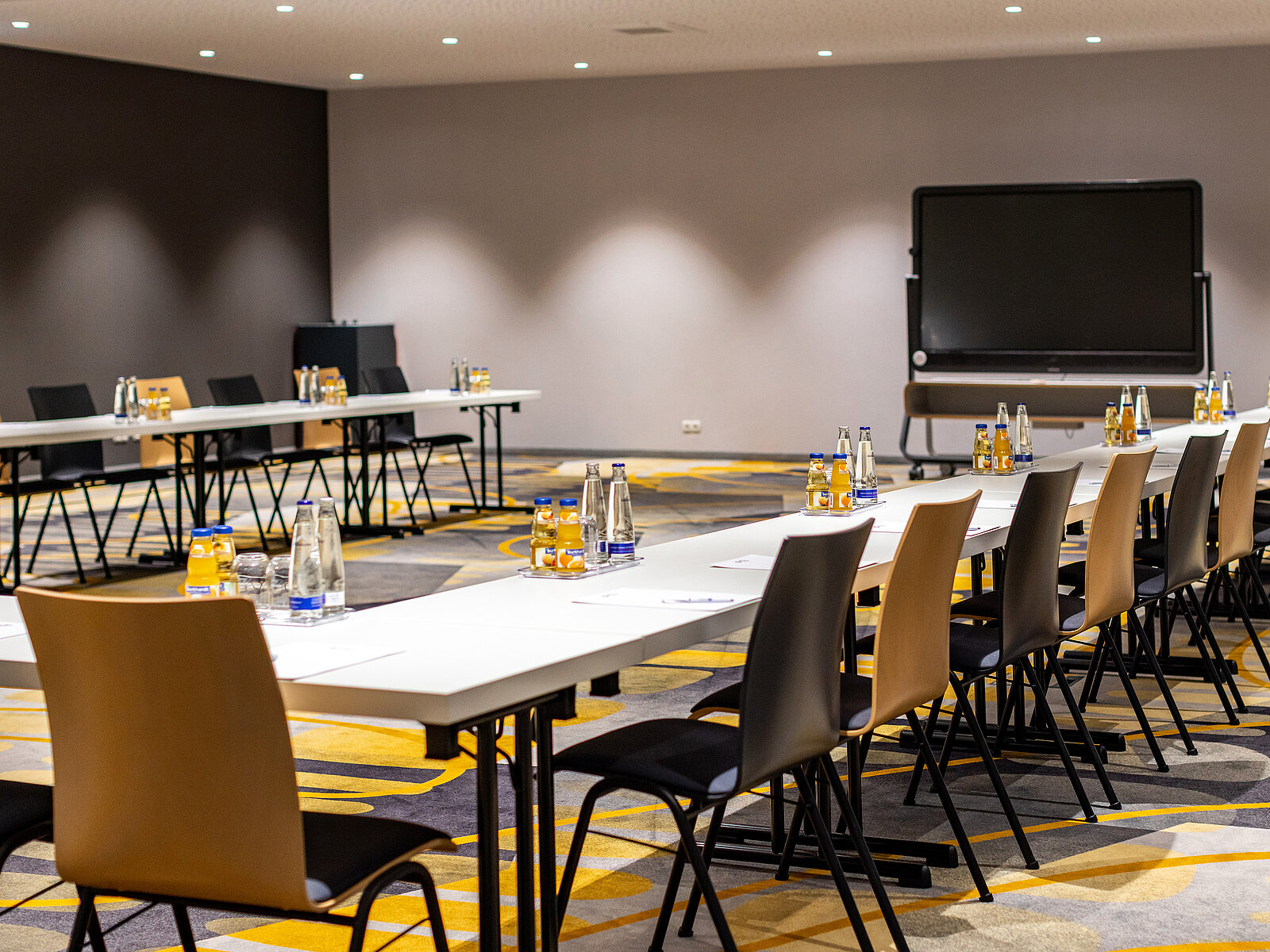 zeiflekoch hotel maximilian parkhotel, moderner konferenzraum mit tischen aufgestellt in U-Form, holzstühle mit gepolsterter sitzfläche, großer monitor an der wand montiert