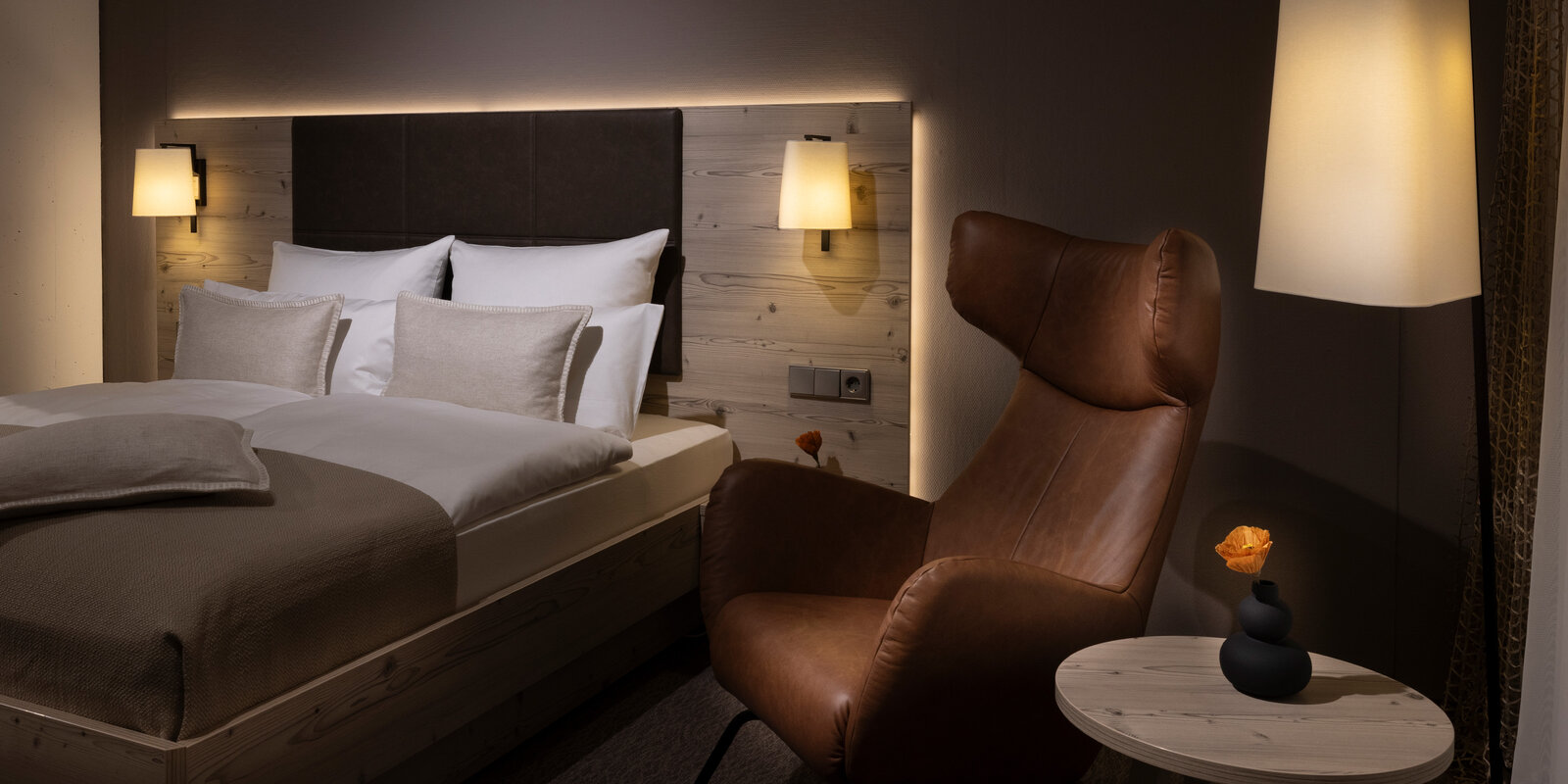 gedämpfte Lichtstimmung in einem Hotelzimmer mit Holzmöbeln und hellbraunem Ledersessel