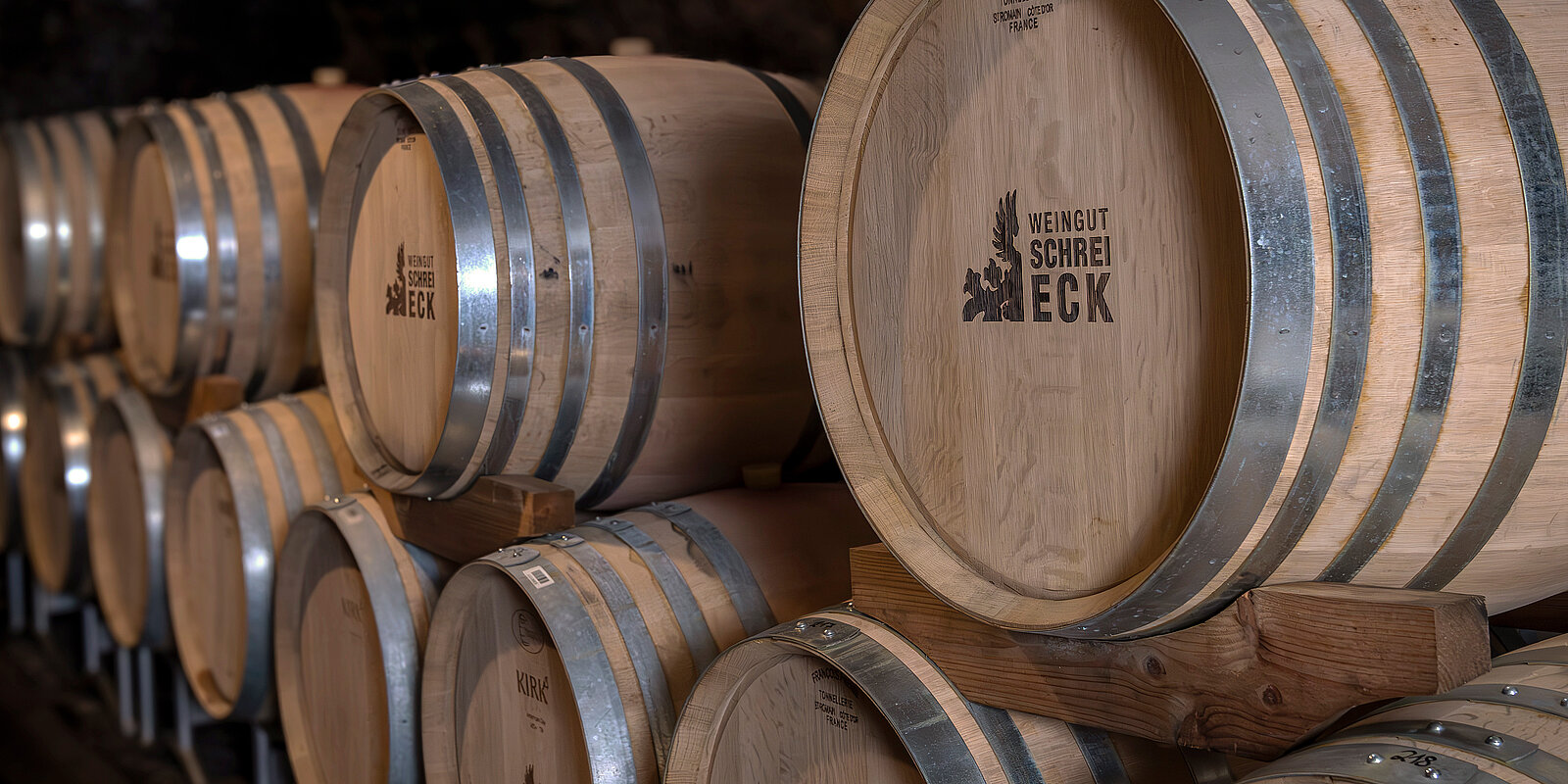 Eine Reihe von Holzfässern in einem Weinkeller, mit dem Schriftzug "Weingut SchreiEck" auf den Fassdauben. Die Fässer sind sorgfältig gestapelt und geben einen Eindruck von Tradition und Handwerk in der Weinproduktion.