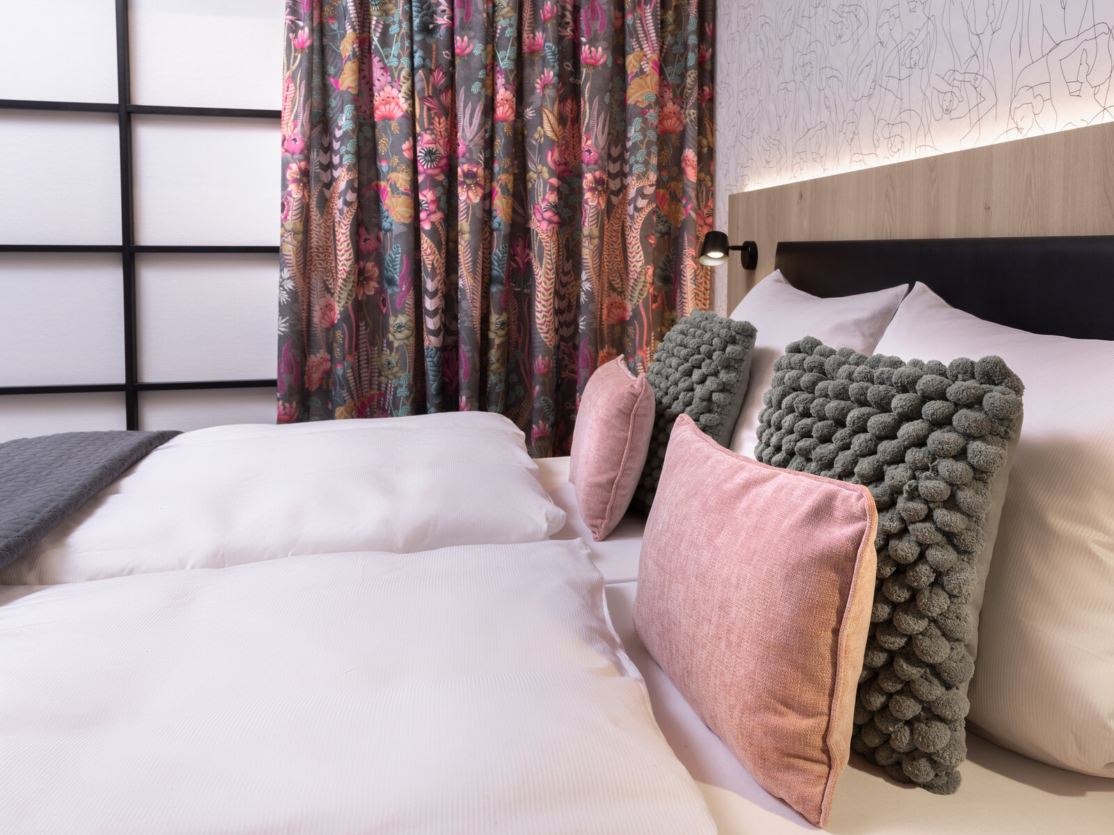 zieflekoch musterzimmer zenit, modernes Schlafzimmer mit einem Boxspring-Doppelbett mit Rückwand in Holzoptik, Vorhänge mit Blumenmuster, Zierkissen in rosa und olivgrün liegen auf dem Bett